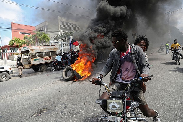 People drive past a burning blockade as demonstrators hold a protest calling for the resignation of Haitian Prime Minister Ariel Henry outside the Canadian Embassy, in Port-au-Prince, Haiti, February 25.
Mandatory Credit:	Ralph Tedy Erol/Reuters via CNN Newsource