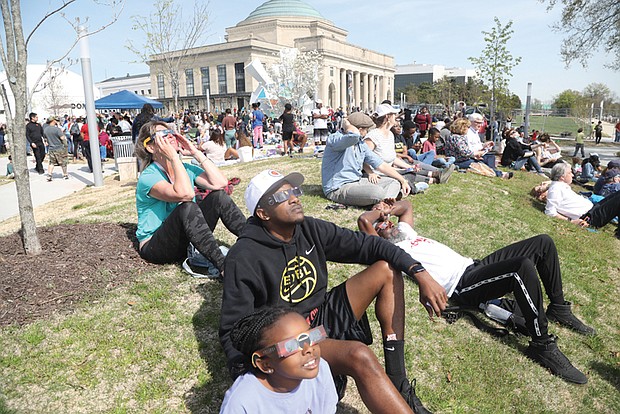Richmonders Avery Scott, center, and his 9-year-old daughter, Zuri Scott, watched the partial solar eclipse Monday, April 8 on the lawn of the Science Museum of Virginia.