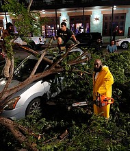 Rapper Trae tha Truth, in yellow, cuts fallen tree limbs on top of a car in the aftermath of a severe thunderstorm that passed through Houston on Thursday.
Mandatory Credit:	David J. Phillip/AP via CNN Newsource