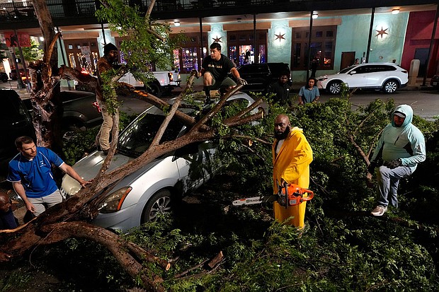 Rapper Trae tha Truth, in yellow, cuts fallen tree limbs on top of a car in the aftermath of a severe thunderstorm that passed through Houston on Thursday.
Mandatory Credit:	David J. Phillip/AP via CNN Newsource