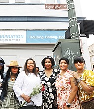 Michon Johnson Moon holds flowers as she stands with her and her late husband August Moon’s daughters, Dr. Sesha Joi Moon, Enjoli Moon, Tiffany Diamond, Rochelle Britton Allen, and Sidell Britton, beneath the newly unveiled honorary street sign at the corner of 12th and Hull streets in South Side on Aug. 3. August Moon, often called the “Mayor of South Side,” among other monikers, died on July 12 last year. The Moon family presented a $10,000 check to Richmond Public Schools Superintendent Jason Kamras to create the August and Michon Moon Endowed Scholarship Fund.