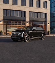 Front 3/4 view of the 2025 Cadillac ESCALADE IQ Sport 2 in Black Raven with a building in the background.