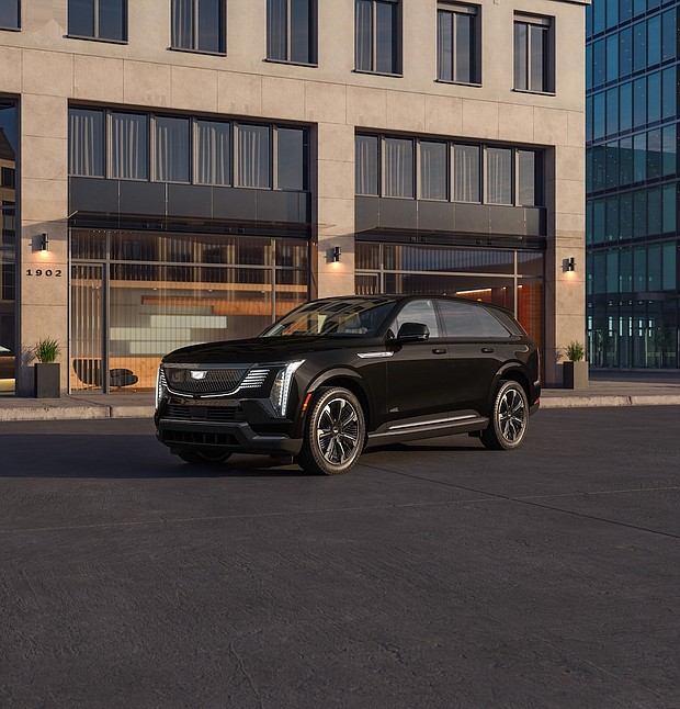 Front 3/4 view of the 2025 Cadillac ESCALADE IQ Sport 2 in Black Raven with a building in the background.
