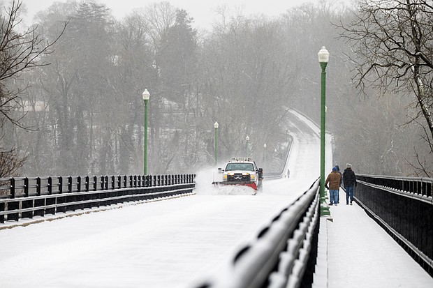 A snow plow clears the Nickel Bridge as two pedestrians walk the span on Feb. 19. The bridge was closed due to the winter weather.