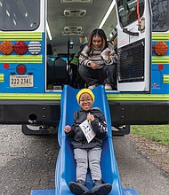 Six-year-old Titus Vaughn slides down from the Lit Limo after picking out a book as student Andie Butler looks on.