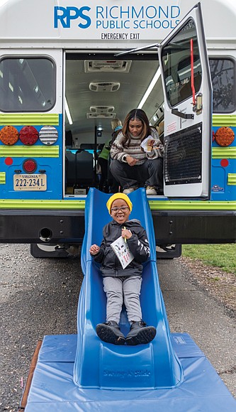 Six-year-old Titus Vaughn slides down from the Lit Limo after picking out a book as student Andie Butler looks on.