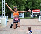 April Burwell jumps for joy in front of the finish line after completing the Bust the Banks Half Marathon trail run at Dominion Energy Riverrock on Sunday, May 18. Her 19-month-old son, Julian, stands grounded beside her, taking it all in.