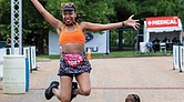 April Burwell jumps for joy in front of the finish line after completing the Bust the Banks Half Marathon trail run at Dominion Energy Riverrock on Sunday, May 18. Her 19-month-old son, Julian, stands grounded beside her, taking it all in.