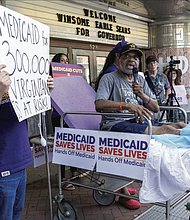 Tony Hedgepeth, a home care worker, speaks from a hospital gurney during a protest outside the Hippodrome. The gurney symbolized how proposed Medicaid cuts could threaten access to care for thousands of Virginia families.