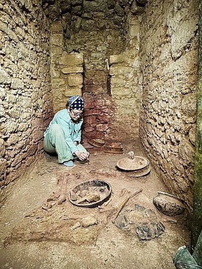 Diane Z. Chase in the tomb of Te K’ab Chaak with vessels in the foreground and jadeite mask to the left and the south wall niche./