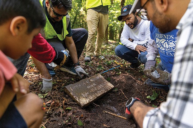 Ahsan Khan, left, and Umer Sindhu, right, along with other members of the Ahmadiyya Muslim Community and Friends of East End Cemetery, wash a newly uncovered gravestone.
