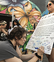 Outside Diversity Richmond on Tuesday, July 15, ahead of a community town hall, Stephanie Foreman holds a sign for Logan Wade to sign. The message supports a Diversity Richmond employee who reported being sexually assaulted and subjected to racism by a coworker.