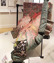 The Jefferson Davis statue, erected in 1907 on Monument Avenue and pulled down by protesters on June 10, 2020, is shown as part of a temporary exhibit at The Valentine. The former Confederate leader appears splattered with pink paint, with a blackened face and a dent on the back of the head from the 2020 protest.