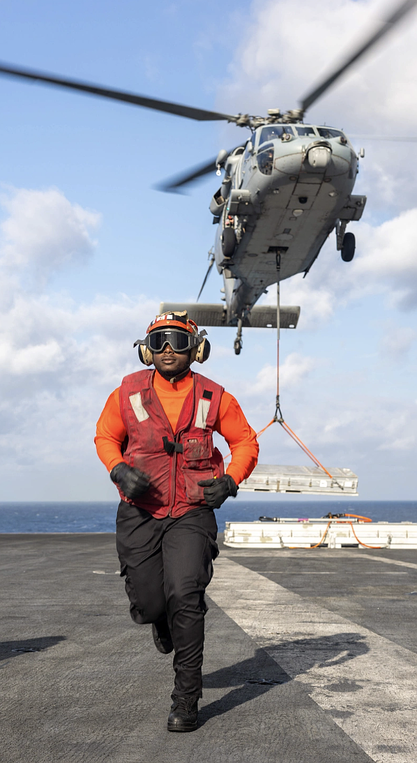 Aviation Ordnanceman 3rd Class Jader Jamecia, a native of Houston, takes position as an MH-60S Sea Hawk helicopter, assigned to the "Dragonslayers" of Helicopter Sea Combat Squadron (HSC) 11, transports ordnance to the Lewis and Clark-class supply ship USNS Robert E. Peary (T-AKE 5) from the flight deck of the Nimitz-class aircraft carrier USS Harry S. Truman (CVN 75) during an ammunition offload. Truman is currently underway in the Atlantic Ocean. (Photo by Mass Communication Specialist 2nd Class Logan McGuire)