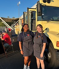 Addison Bryce, left, and Alexis Phillips stand in front of the Dawg Treats food bus at Goochland High School, where they sell globally inspired cuisine during football games.