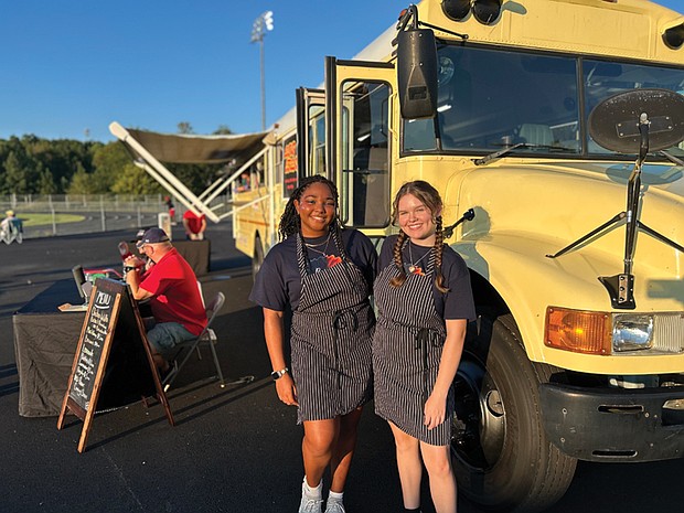 Addison Bryce, left, and Alexis Phillips stand in front of the Dawg Treats food bus at Goochland High School, where they sell globally inspired cuisine during football games.