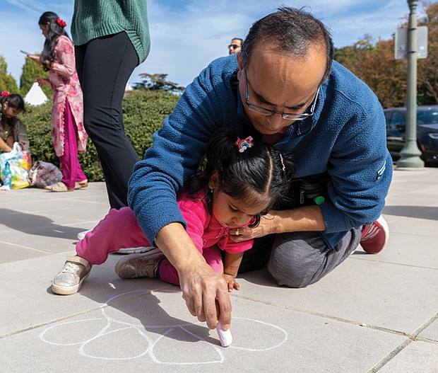 Colors of culture-Vishal S. helps his 3-year-old daughter, Aanya, outline a flower for a rangoli sand design during the Diwali Music & Arts Festival on Oct. 18 at the Virginia Museum of History & Culture. The festival celebrated traditional Indian culture and featured land folk dances, a Ramayan puppet show, a fashion show, henna and rangoli stations and an arts bazaar. (Julianne Tripp Hillian/Richmond Free Press)