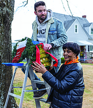 Chris Miller hangs a wreath from a ladder as Dolores W. Whitaker, 90, looks on along the 1300 block of Hampton Street. Whitaker has decorated the trees on her block for the past 30 years.