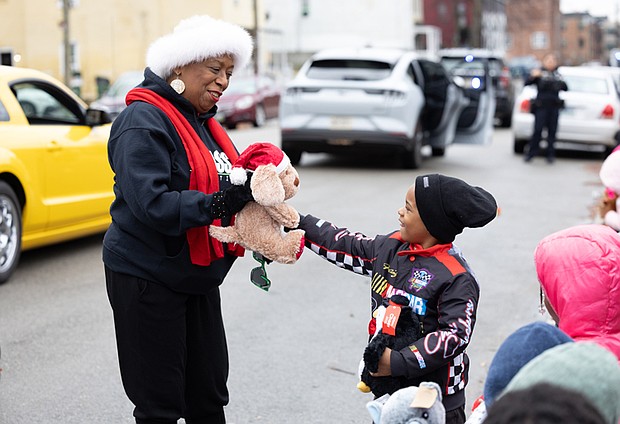 Holiday convoy delivers smiles in Gilpin Court-During the FRIENDS Association for Children’s annual holiday vehicle parade Tuesday morning along St. John Street in Gilpin Court, vehicles from Richmond Fire and Police, Richmond Ambulance and local car clubs circle neighborhoods in Gilpin Court and Church Hill, distributing stuffed animals and other gifts to children along the route. Richmond School Board member Cheryl Burke hands a stuffed reindeer to Sha’vez Pressley, 6, and other children along St. John Street in Gilpin Court. (photo by Julianne Tripp Hillian/Richmond Free Press)