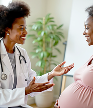 African American doctor consults pregnant woman in clinic. Smile, talk about maternal health, wellness. Black physician gives prenatal care advice to future mother. Expecting woman holds belly