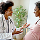 African American doctor consults pregnant woman in clinic. Smile, talk about maternal health, wellness. Black physician gives prenatal care advice to future mother. Expecting woman holds belly