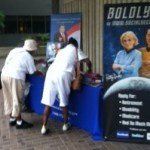 The SSA recently announced it will reduce its public service hours by 30 minutes at field offices nationwide on Aug 15. In the photo: Two individuals visit a SSA information table at a community event on July 22, 2011.  (Photo Courtesy of Social Security Administration)